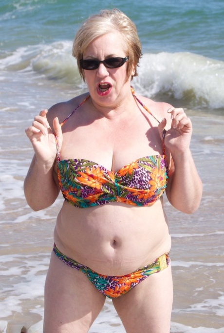 Mature UK woman Speedy Bee wears sunglasses while getting naked at the beach 25573663