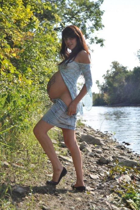 Solo girl Brianna exposes her pregnant belly on rocky shore beside a river 99676339