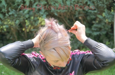 Blonde girl fixes her ball gag while restrained in a nylon tracksuit on a lawn 43205234