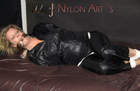 Blonde woman is tied up with rope while gagged in black nylon rainwear 52586794